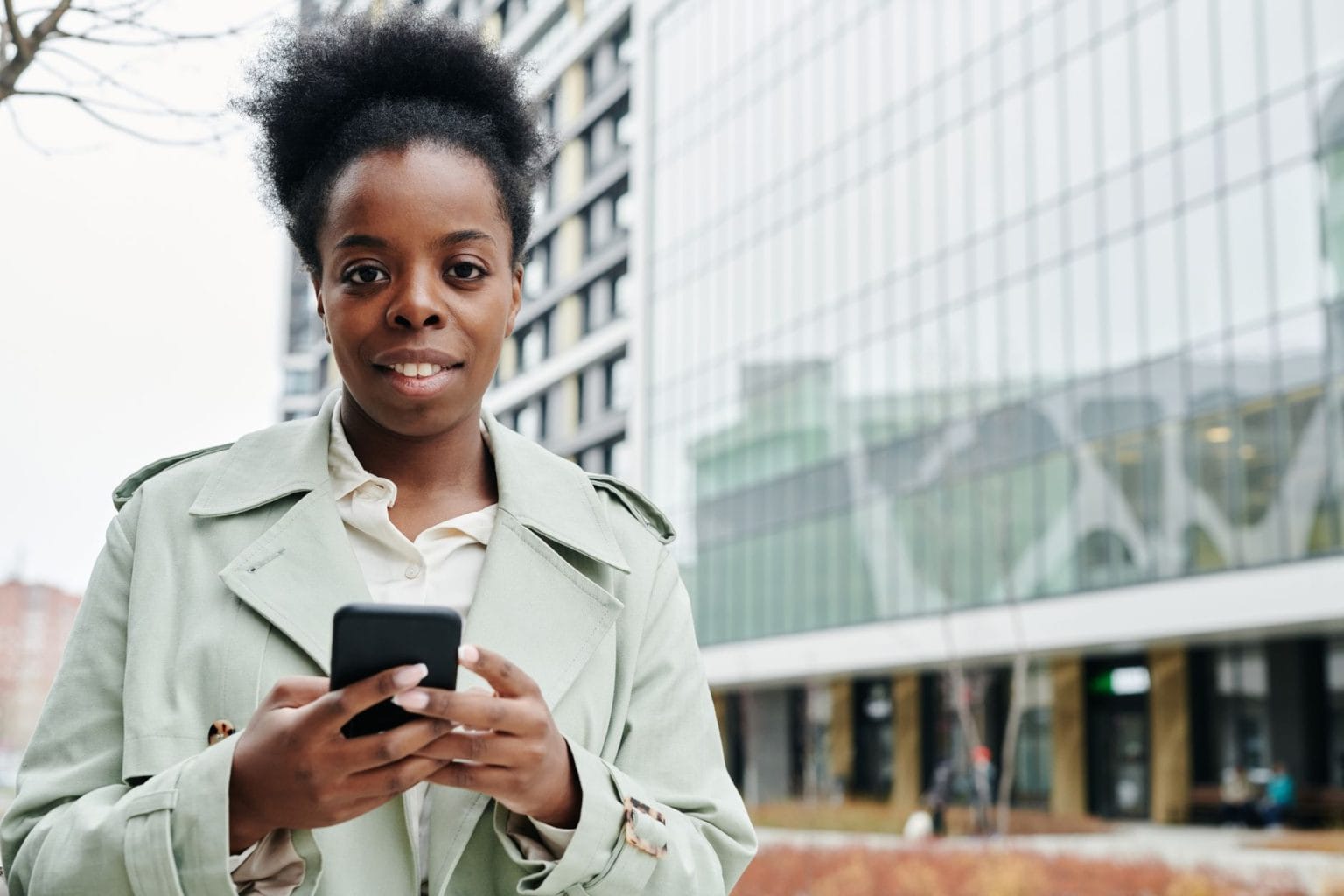 Profissional negra usando o celular em frente a um edifício de escritórios.