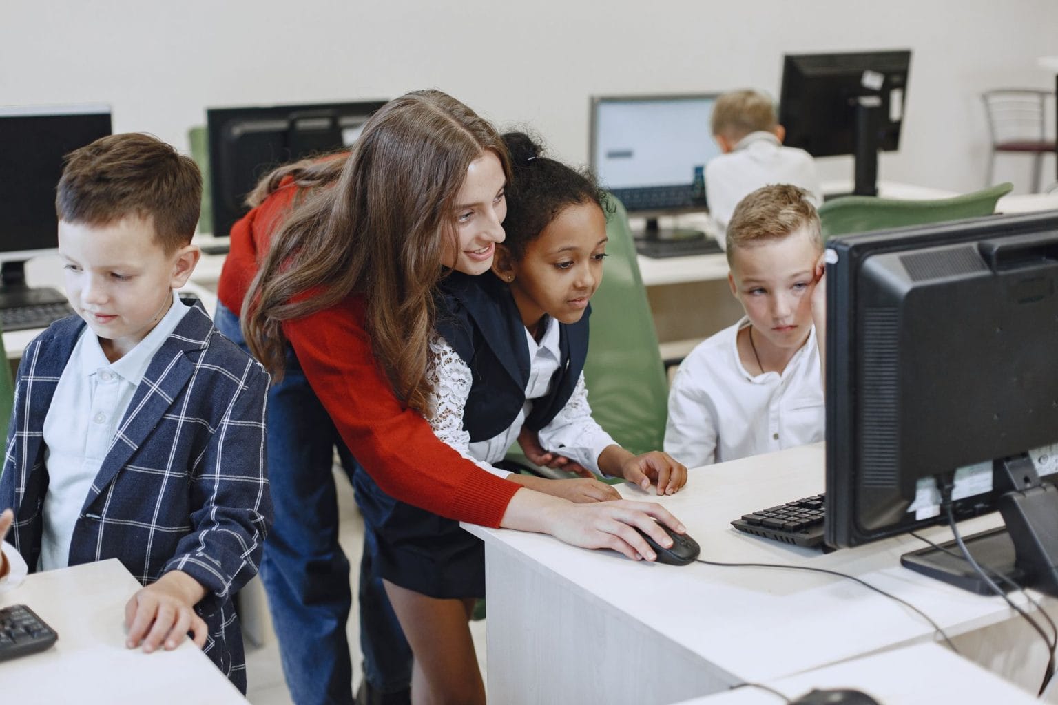 Professora orienta alunos durante uma atividade com computadores em uma sala de aula moderna.